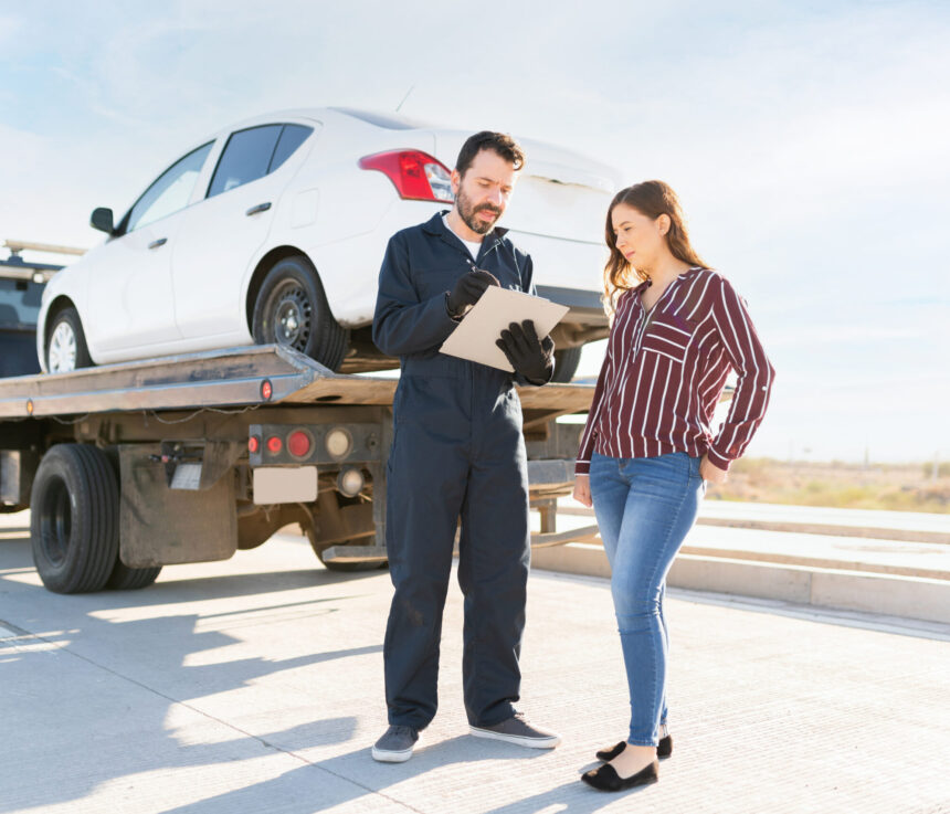 Male tow truck operator with a chart charging a young woman the services for towing her dead car off the highway